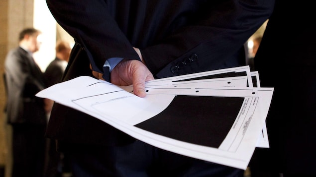 Un fonctionnaire fédéral tient dans une main des feuilles d'un document censuré.