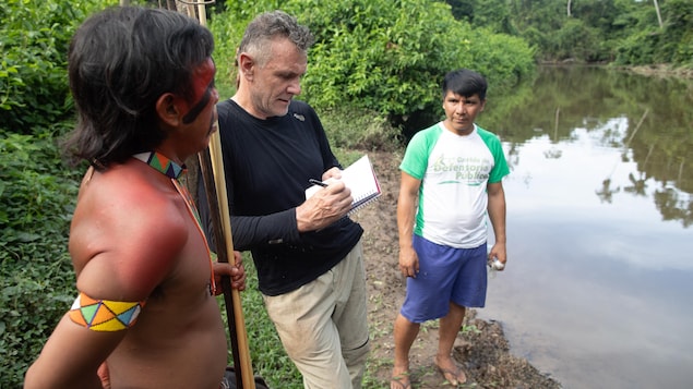 Dom Phillips prend des notes aux côtés de deux Autochtones en Amazonie.