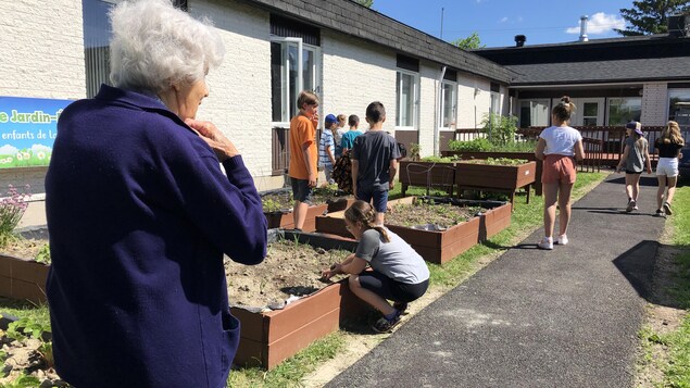 Une personne âgée regarde des jeunes dans un jardin.
