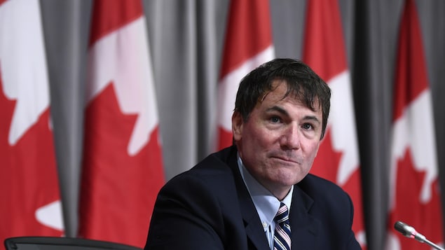 Le ministre LeBlanc est assis à une table, derrière un micro. Derrière lui se trouvent des drapeaux du Canada.