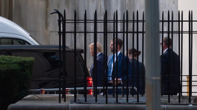 Donald Trump et d'autres personnes, qu'on aperçoit derrière une clôture.