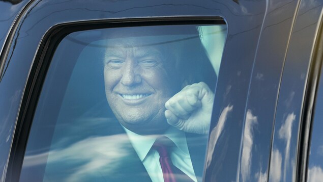 Donald Trump, souriant et le poing levé, vu à travers la vitre d'une voiture à son arrivée à Mar-a-Lago, en Floride.