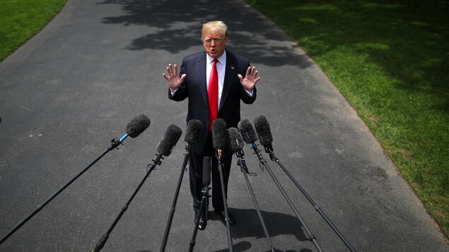 Le président américain Donald Trump debout en conférence de presse, devant des micros tendus vers lui.