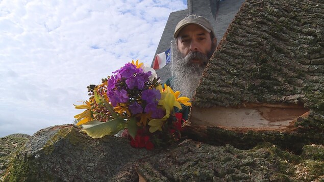Un bouquet de fleurs et un petit drapeau acadien sur l'arbre couché sur le côté.