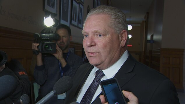 Photo de Doug Ford qui est entouré de micros et de caméras dans un corridor de l'Assemblée législative. Photo de Doug Ford qui est entouré de micros et de caméras dans un corridor de l'Assemblée législative.