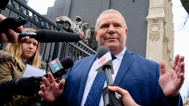 Doug Ford, entouré de micros, sourit aux journalistes. Doug Ford, entouré de micros, sourit aux journalistes.