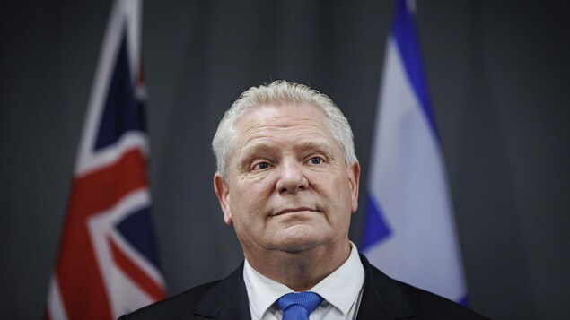 Le premier ministre regarde à l'horizon devant deux drapeaux lors d'un point de presse.