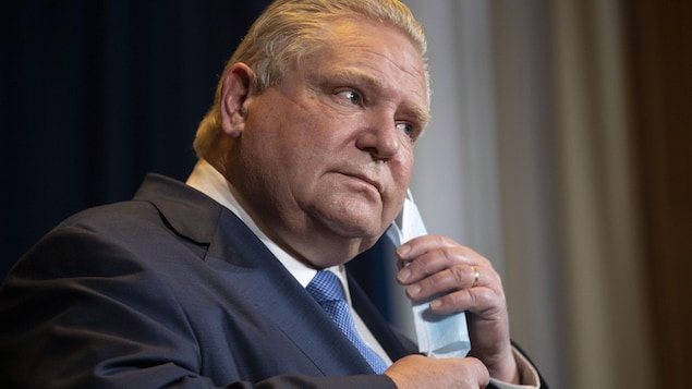 Doug Ford takes off his mask before speaking at a press briefing.