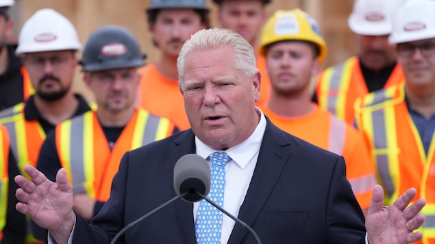 Doug Ford parlant à un lutrin devant des travailleurs de la construction portant gilet orange et casque sur un chantier de Hamilton le 24 août 2026.