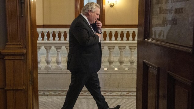 Le premier ministre Doug Ford parle au téléphone en marchant dans un couloir à Queen's Park.