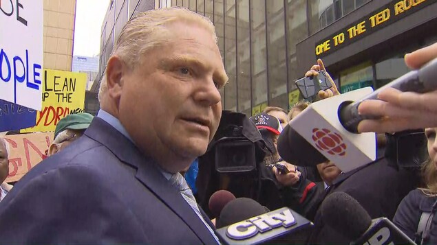 Doug Ford en complet est entouré de micros de journalistes Doug Ford en complet est entouré de micros de journalistes