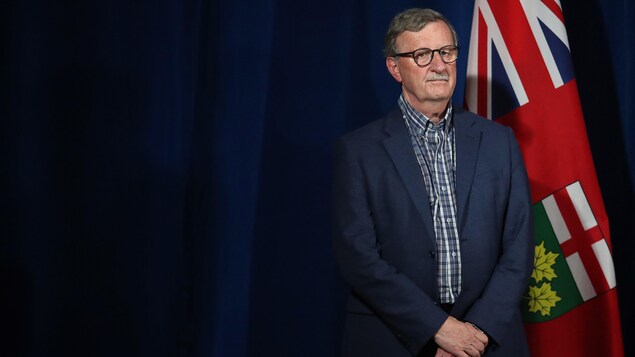 Dr David Williams écoute le premier ministre lors d'une conférence de presse.