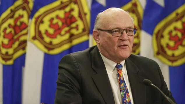 Robert Strang devant des drapeaux de la Nouvelle-Écosse.