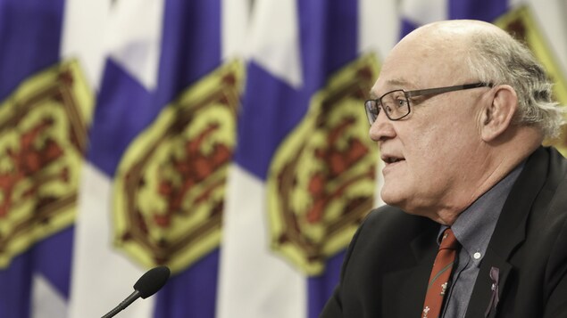 Robert Strang de profil devant des drapeaux de la Nouvelle-Écosse.