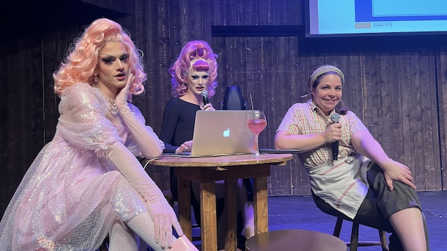 Deux drag queens et une actrice habillée en personnage de la Sagouine, sur scène.