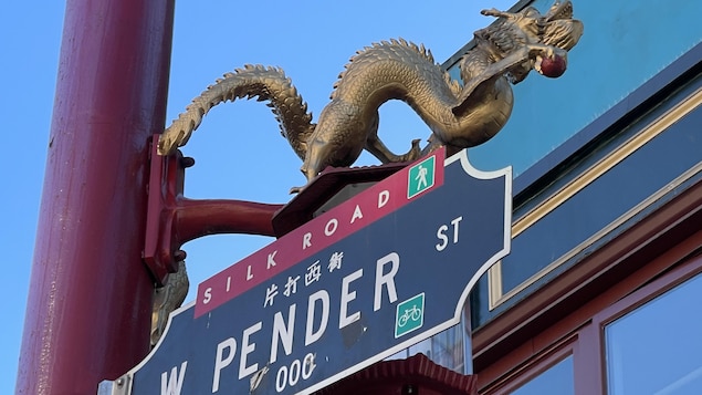 Une pancarte affichant West Pender Street est accroché à un lampadaire sur lequel est perchée une sculpture de dragon.