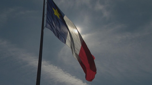 Un drapeau acadien qui flotte dans le vent avec les rayons de soleils qui passent au travers.