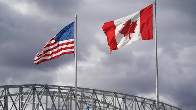 Les drapeaux des États-Unis et du Canada flottent devant un ciel sombre.