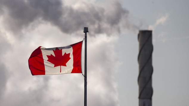 Un drapeau canadien avec, en arrière-plan, de la fumée qui sort d'une cheminée.