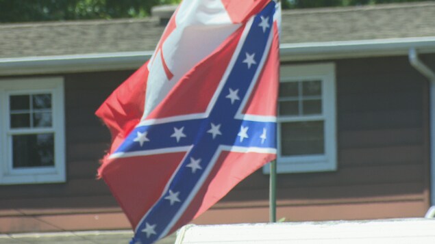 Un drapeau canadien et un drapeau confédéré flottent au vent devant une maison.