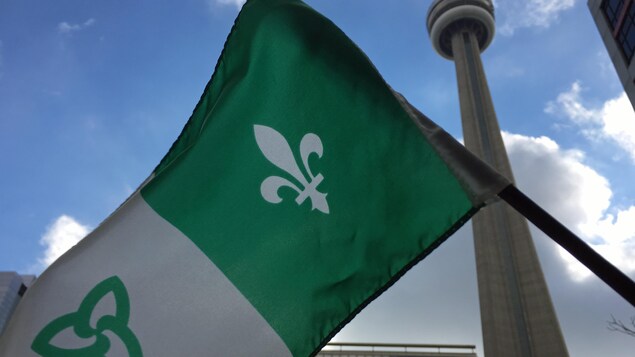 Un drapeau franco-ontarien tenu devant la Tour CN à Toronto.