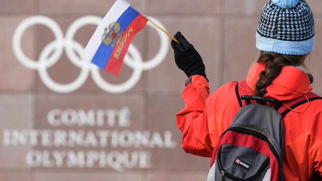 Une femme tient un petit drapeau de la Russie devant les bureaux du Comité international olympique.