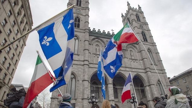 Des personnes portant des drapeaux du Québec et des patriotes, devant la basilique.