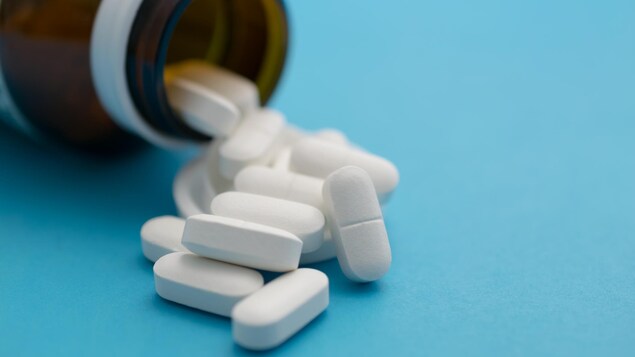 Gros plan sur des capsules de médicaments blanches à la sortie d'une bouteille ambrée couchée sur le côté.