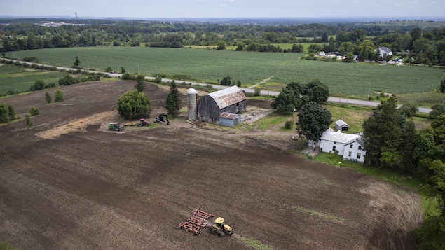 Vue aérienne d'une ferme et d'un tracteur dans un champ. Au fond, des espaces verts.