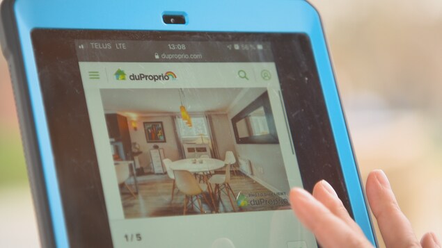 Des doigts balaient la surface d'une tablette où on aperçoit une photo de la salle à manger d'un condo à louer.