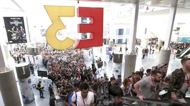 Une photo montrant des centaines de personnes faisant la queue pour gravir les escaliers roulants, dans l'entrée principale du centre des congrès de Los Angeles. Un énorme logo de l'E3 est suspendu au-dessus des escaliers roulants.