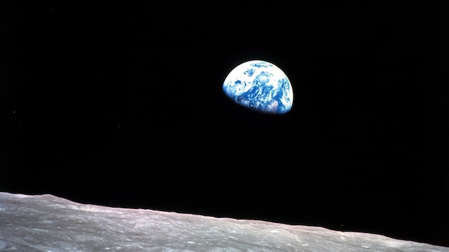 On voit la surface de la Lune, grise et avec des cratères, et au loin, un peu plus de la moitié de la Terre.