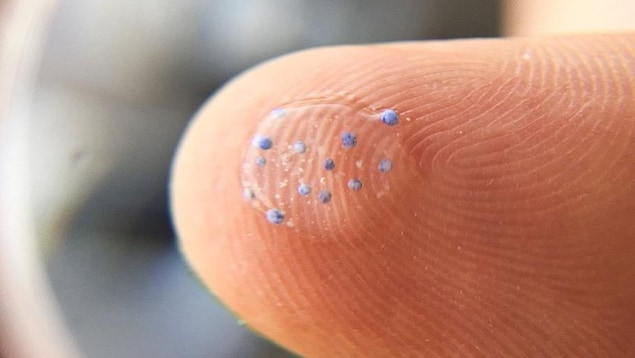 Gros plan d'une goutte d'eau sur un doigt qui contient des minuscules billes de plastique.