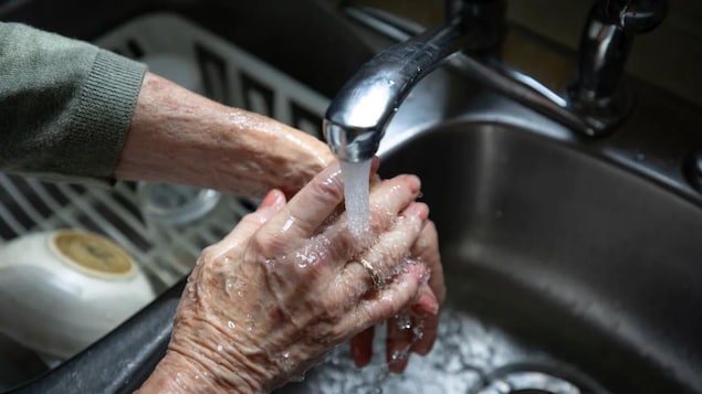De l'eau coule du robinet sur des mains d'une personne âgée.