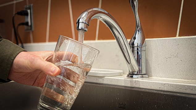 Une personne remplit un verre d'eau. 