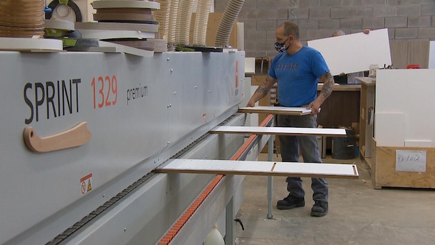 Un homme tient une planche près d'une machine.