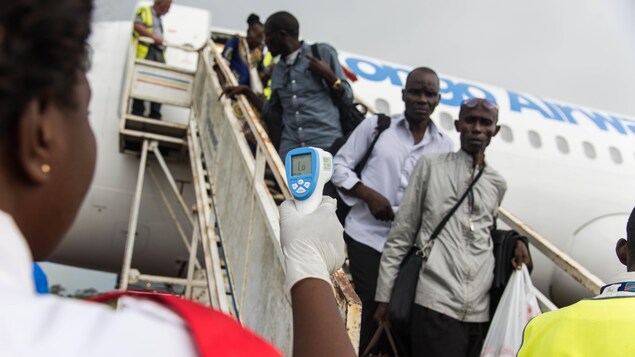 Une femme pointe un thermomètre infrarouge vers des passagers descendant d'un avion. Une femme pointe un thermomètre infrarouge vers des passagers descendant d'un avion.