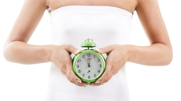 Une femme tient une horloge contre son ventre. Une femme tient une horloge contre son ventre.