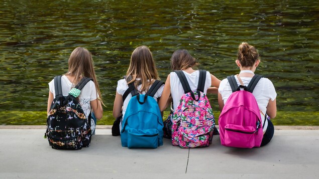 Des jeunes filles munies de sac-à-dos colorés sont assises près d'une fontaine d'eau.