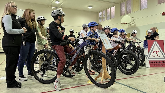 Une vingtaine de jeunes sont rassemblés dans le gymnase de leur école, enfourchant leur bicyclette.