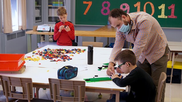 Deux jeunes et un enseignant dans une classe. Ils apprennent à l'aide de blocs légo.