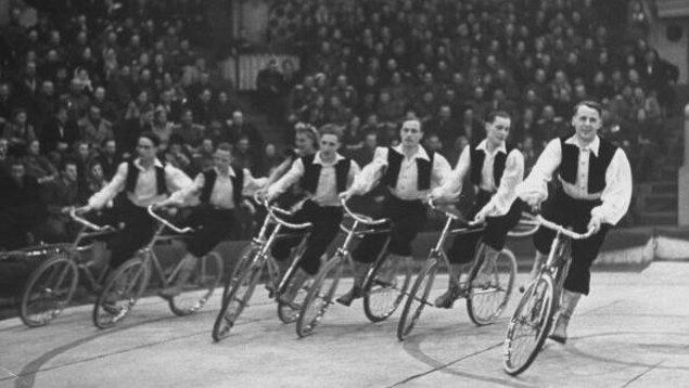 Sept artistes sur des vélos tournent en rond autour d'une piste dans un cirque Sept artistes sur des vélos tournent en rond autour d'une piste dans un cirque