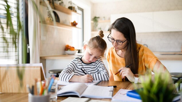  Une mère surveille sa petite fille qui fait ses devoirs scolaires.