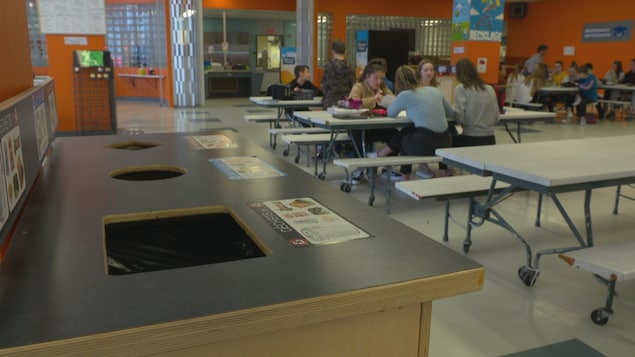 Un îlot de recyclage, poubelle et compostage dans une cafétéria d'école avec des élèves qui sont assis aux tables.