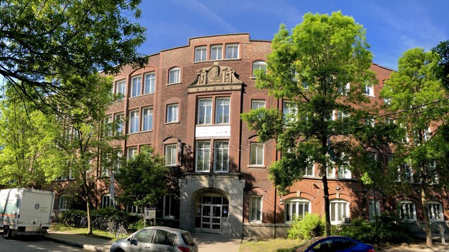 Une école de plusieurs étages vue de l'extérieur, entourée d'arbres et de quelques voitures garées.
