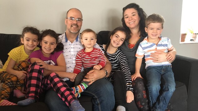 Des parents et leurs cinq enfants sont assis sur un divan, souriants.