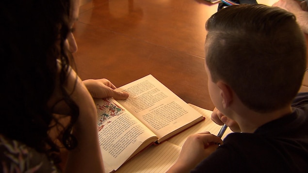 Une mère aide son fils dans ses lectures. Ils sont installés côte à côte à une table de cuisine.