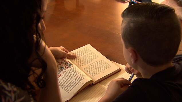 Une mère aide son fils dans ses lectures. Ils sont installés côte à côte à une table de cuisine.