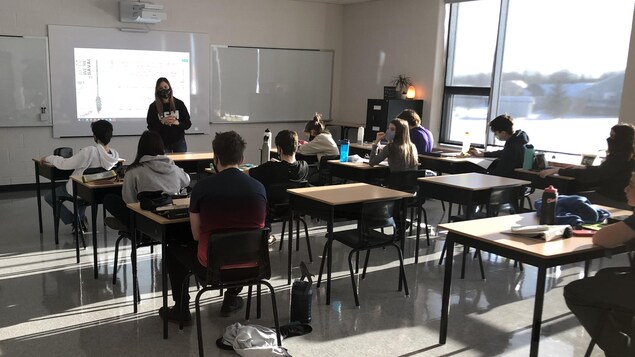 Des élèves écoutent une enseignante en classe.