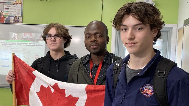 Des élèves se tiennent debout avec leur enseignant, ils portent un drapeau canadien. 